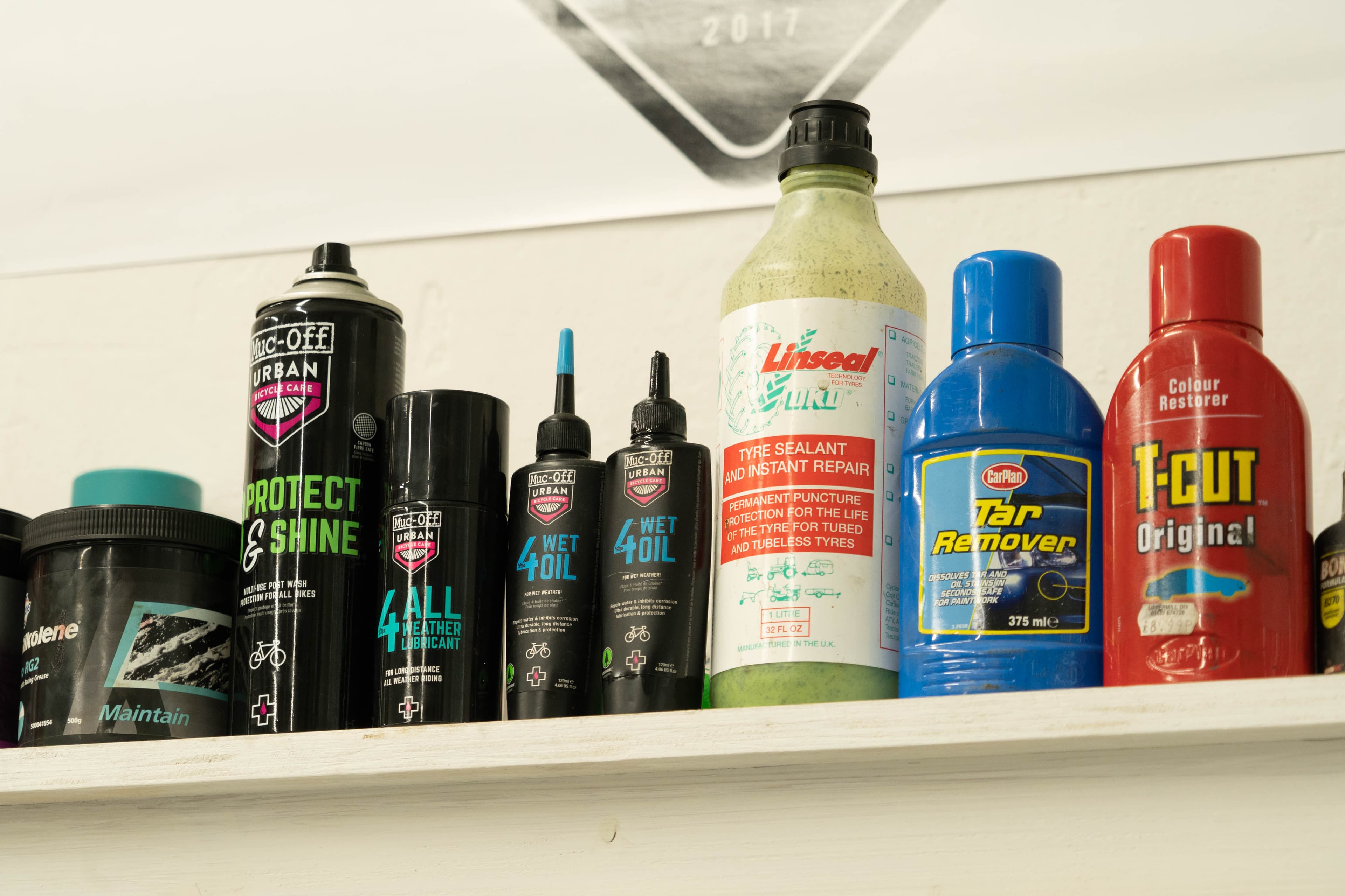 A workshop shelf with bicycle protectant, lubricant and tire sealant beside unrelated automotive tar remover and color restorer